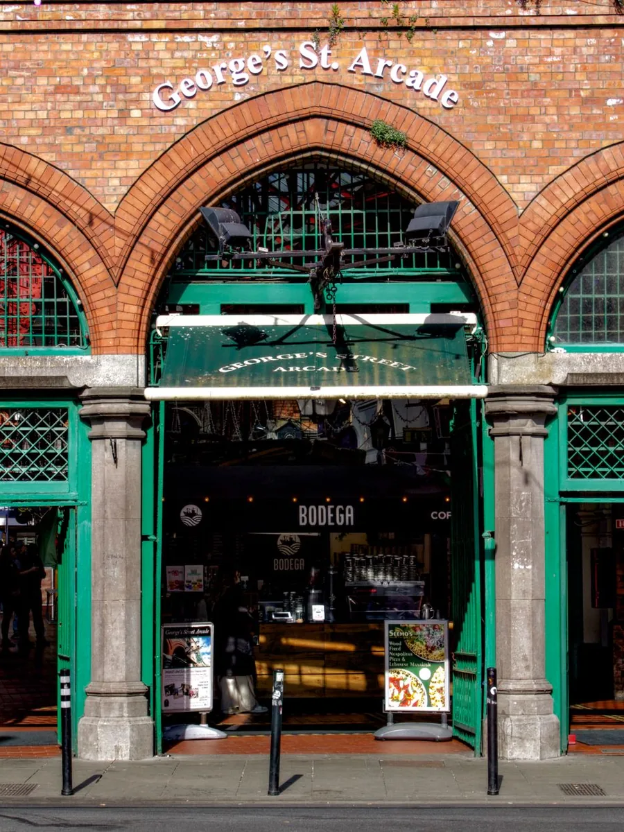 The red-brick arched entrance of George’s Street Arcade in Dublin, with green-painted doors and columns
