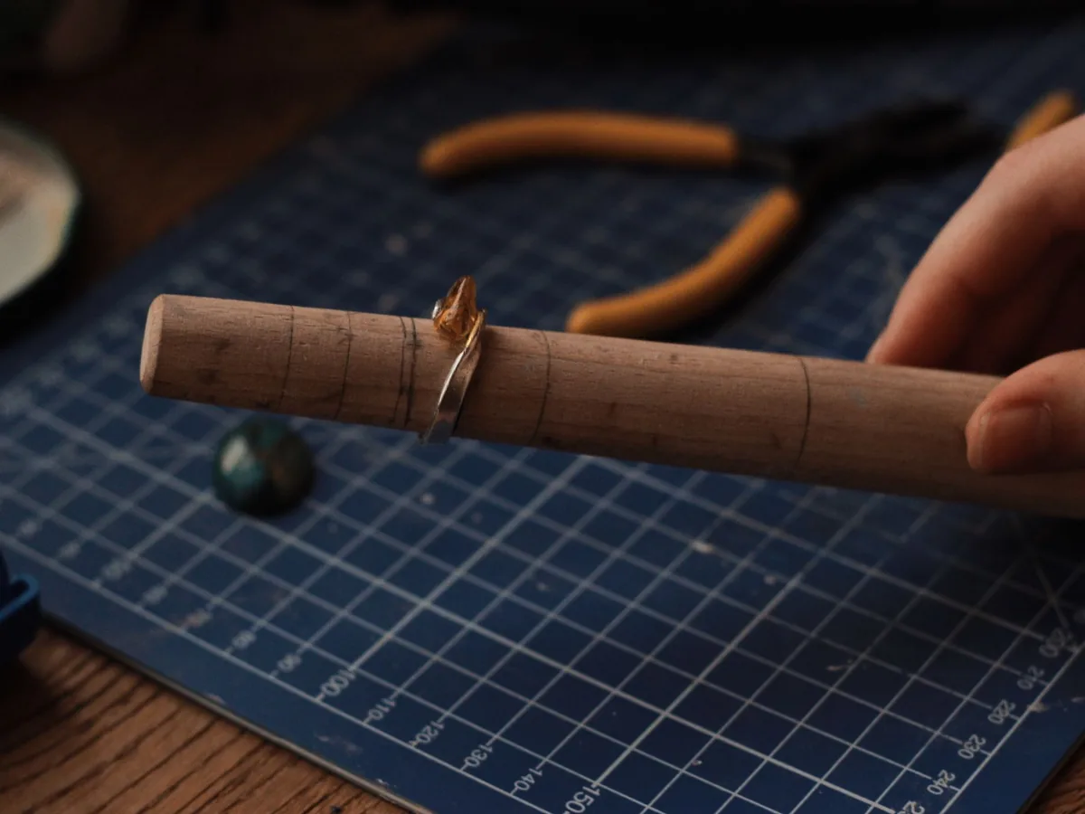 A ring resting on a wooden ring mandrel beside pliers on a blue cutting mat