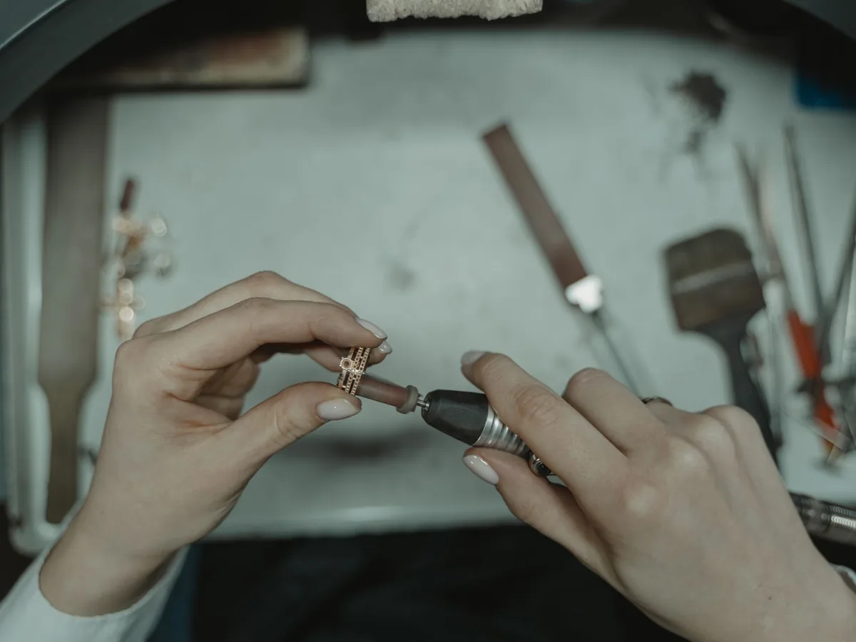 Two hands holding a small ring against a rotary polishing tool on a jeweller’s bench